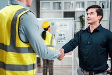 An engineer with a protective vest handshake with an investor in his office. Following a successful meeting, employee and employer form a partnership.