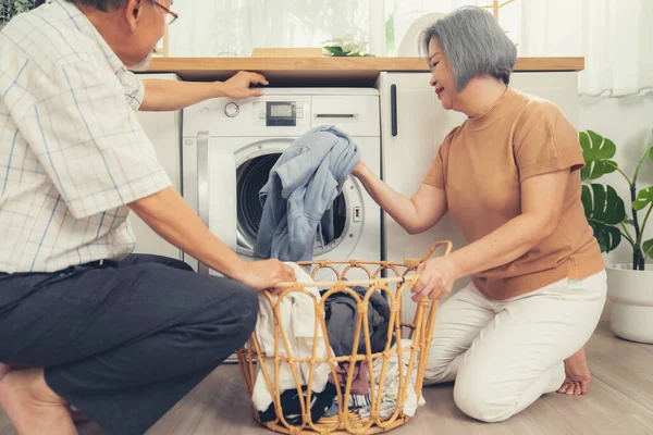 Senior couple working together to complete their household chores at the washing machine in a happy and contented manner. Husband and wife doing the usual tasks in the house.