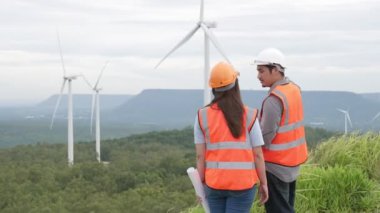 Erkek ve kadın mühendisler kırsal kesimdeki bir tepenin tepesinde ya da dağda rüzgar çiftliğinde çalışıyorlar. Yenilenebilir ve sürdürülebilir enerjinin gelecekteki üretimi için yenilikçi idealler.