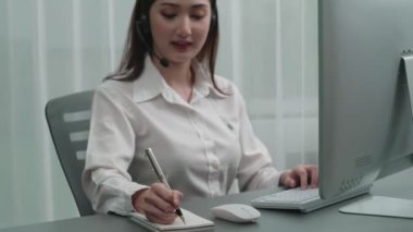 Masasında dizüstü bilgisayarla çalışan kulaklık ve mikrofon takan Asyalı müşteri destek operatörü. Hevesli kadın çalışanlar müşteri hizmetleri sunuyor, destekleyici çağrı merkezi temsilcisi müşterilere yardım ediyor.