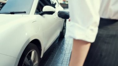 İlerici iş kadını şehir merkezinde dolaşmadan önce şarj cihazından elektrikli arabasına şarj prizi takıyor. Çevre dostu şarj edilebilir araba, sürdürülebilir ve temiz enerjiyle çalışıyor..