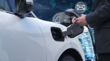 İlerici işadamı, arka planda ağ sembolleri olan şehir ve İnternet 'ten gelen yenilenebilir enerji kaynaklı şarj cihazını elektrikli aracına yüklüyor. Modern çevre dostu kavram.