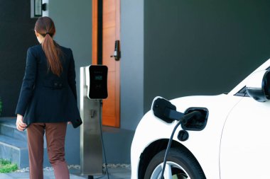 Progressive woman install cable plug to her electric car with home charging station. Concept of the use of electric vehicles in a progressive lifestyle contributes to clean environment.