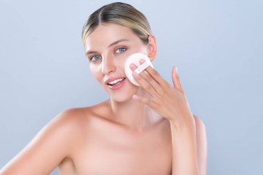 Alluring beautiful female model applying powder puff for facial makeup concept. Portrait of flawless perfect cosmetic skin woman put powder foundation on her face in isolated background.