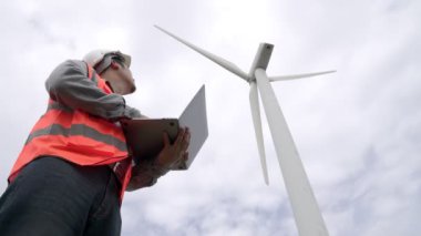 Gökyüzü arka planına sahip bir rüzgar türbini üzerinde çalışan mühendis. Yenilenebilir ve sürdürülebilir enerjinin gelecekteki üretimi için yenilikçi bir ideal. Rüzgar türbininden enerji üretimi.