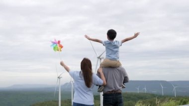 İlerici mutlu aile kavramı rüzgâr türbini çiftliğinde eğleniyor. Rüzgar türbini jeneratörüyle gelen elektrik jeneratörü kırsal bölgede tepe ve ufukta dağ var..