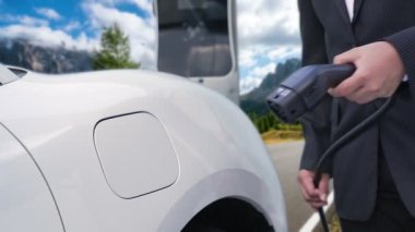 İş dünyasındaki yenilikçi adam elektrikli arabasını dağlarla dolu bir kırsal kesimdeki şarj istasyonundan alıyor. Yol yolculuğu, EV arabalı macera yenilenebilir enerjiyle çalışıyor..