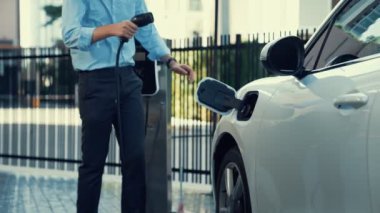 İlerici işadamı, şehir merkezinde dolaşmadan önce şarj cihazından elektrikli arabasına şarj prizi takıyor. Çevre dostu şarj edilebilir araba, sürdürülebilir ve temiz enerjiyle çalışıyor..