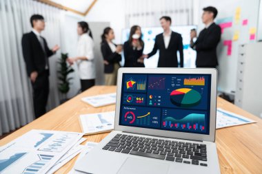 Focus laptop monitor display dashboard report by business intelligence, analyzed financial data for planning market strategy with blur background of standing office worker discussing in harmony office