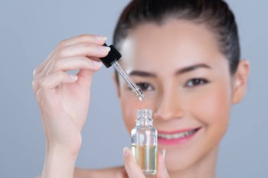 Focus cannabis extracted oil bottle with dropper lid holding by blurred glamorous beautiful asian woman with perfect clean skin and soft smooth makeup in isolated background.