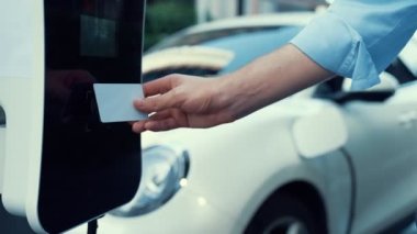 Bir adam kredi kartını, şarj istasyonundaki elektrikli aracının temiz ve sürdürülebilir enerjisini ödemek için kullanıyor. Yenilikçi adam şarj edilebilir aracına güç sağlamak için ödeme yapıyor..