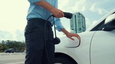 İlerici işadamı, şehir merkezinde dolaşmadan önce şarj cihazından elektrikli arabasına şarj prizi takıyor. Çevre dostu şarj edilebilir araba, sürdürülebilir ve temiz enerjiyle çalışıyor..