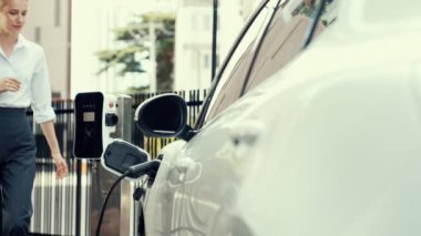 İlerici iş kadını, şehir merkezinde dolaşmadan önce şarj cihazının fişini şarj istasyonundan elektrikli arabasına çekti. Çevre dostu şarj edilebilir araba, sürdürülebilir ve temiz enerjiyle çalışıyor..