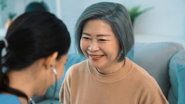 A contented retired senior woman being exterminated by her caregiver with a stethoscope at home. Medical care service, senior care at home.