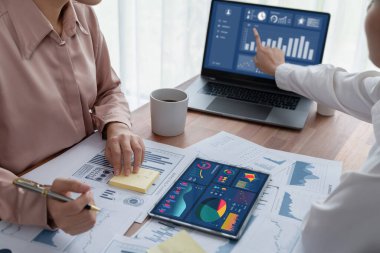 Analist ekip arkadaşı dijital gösterge panelinde finansal verileri tartışır, grafikleri dizüstü bilgisayar ve tablet ekranda analiz eder. Modern ofis pazarlama planlamak için iş zekasını kullanır. Coşkulu.