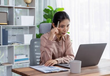 Modern ofis masasındaki Asyalı hevesli genç iş kadını çalışmak ve notlar yazmak için dizüstü bilgisayar kullanıyor. Çalışkan ve çekici ofis hanımı ofisinde bilgisayar defteri üzerinde çalışıyor..