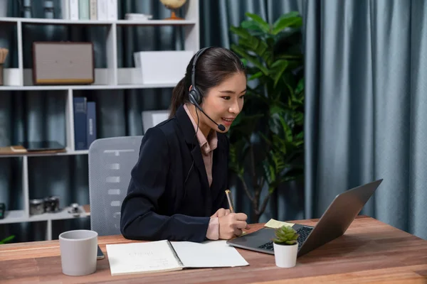 Bilgisayarında mikrofon ve kulaklıkla Asyalı çağrı merkezi çalışıyor. Kadın operatör istisnai müşteri hizmetleri sunar. Destek veren çağrı merkezi ajanı, müşteriye soruşturmada yardım ediyor. Coşkulu.