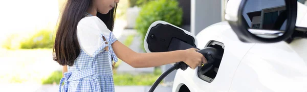 Evプラグを持つ遊び心のある女の子 電気自動車のための持続可能な電源を提供する家庭用充電ステーション 進歩的なライフスタイルのための代替エネルギー — ストック写真