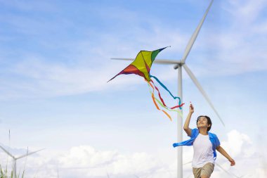 İlerici mutlu kaygısız çocuk konsepti. Yol boyunca koşan ve uçurtma uçuran genç bir çocuk kırsal alanda doğal manzaralı, açık gökyüzü ve güneşli bir gün dağ ve rüzgar türbini arka planında