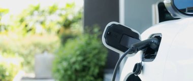 Closeup electric vehicle plugged-in with cable from charging point powered for progressive concept by alternative clean energy rechargeable EV car at home charging station.