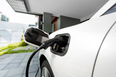 Closeup electric vehicle plugged-in with cable from charging point powered for progressive concept by alternative clean energy rechargeable EV car at home charging station.