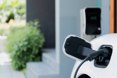 Closeup electric vehicle plugged-in with cable from charging point powered for progressive concept by alternative clean energy rechargeable EV car at home charging station.