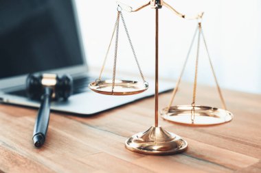 Adalet ve hukuki otoriteyi temsil eden, altın dengeli ölçek ve hukuk bürosunda dizüstü bilgisayarlı tokmak, avukat ve hakimin eşitlik ve adil yargılama kavramını yansıtıyor. denge