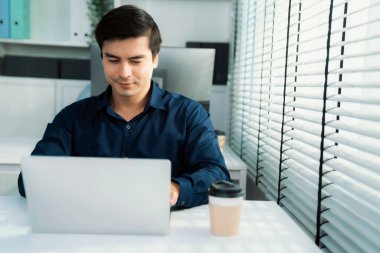 Competent male employee sits at his desk with a cup of coffee. Modern employee working with a drink, recreation during working hours, caffeine for office workers.