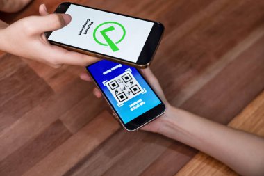 QR kodu parasız ödeme taraması için ekranda gösterilir. Kapalı eller, mobil uygulamadan elektronik işlem yoluyla para aktarmak için akıllı telefonu tutuyor. Hızlı ödeme için barkod teknolojisi. Coşkulu.