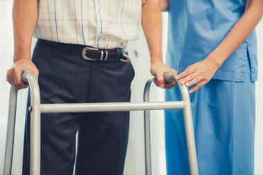 Physiotherapist assists her contented senior patient on folding walker. Recuperation for elderly, seniors care, nursing home.