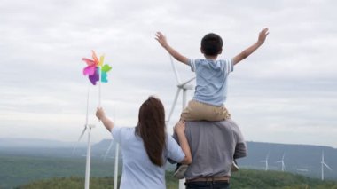 İlerici mutlu aile kavramı rüzgâr türbini çiftliğinde eğleniyor. Rüzgar türbini jeneratörüyle gelen elektrik jeneratörü kırsal bölgede tepe ve ufukta dağ var..