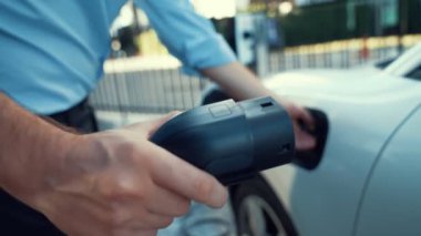 İlerici işadamı, şehir merkezinde dolaşmadan önce şarj cihazından elektrikli arabasına şarj prizi takıyor. Çevre dostu şarj edilebilir araba, sürdürülebilir ve temiz enerjiyle çalışıyor..