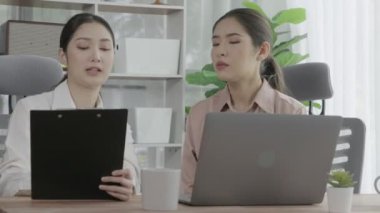 Ofis çalışma alanında birlikte çalışan iki genç hevesli iş kadını. Genç meslektaşlar tartışırken ve dizüstü bilgisayar kullanırken. Modern ofis çalışanları masada birlikte oturuyorlar..