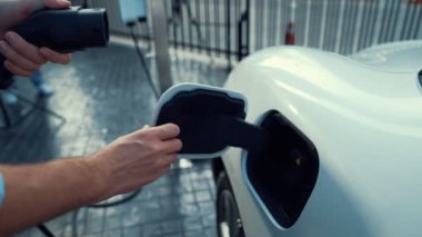 İlerici işadamı, şehir merkezinde dolaşmadan önce şarj cihazından elektrikli arabasına şarj prizi takıyor. Çevre dostu şarj edilebilir araba, sürdürülebilir ve temiz enerjiyle çalışıyor..