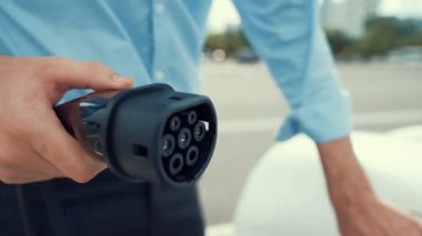 İlerici işadamı, şehir merkezinde dolaşmadan önce şarj cihazından elektrikli arabasına şarj prizi takıyor. Çevre dostu şarj edilebilir araba, sürdürülebilir ve temiz enerjiyle çalışıyor..