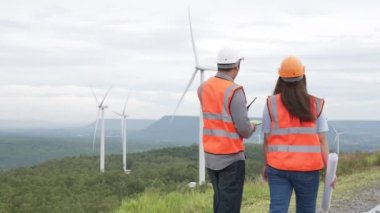Erkek ve kadın mühendisler kırsal kesimdeki bir tepenin tepesinde ya da dağda rüzgar çiftliğinde çalışıyorlar. Yenilenebilir ve sürdürülebilir enerjinin gelecekteki üretimi için yenilikçi idealler.