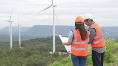 Erkek ve kadın mühendisler kırsal kesimdeki bir tepenin tepesinde ya da dağda rüzgar çiftliğinde çalışıyorlar. Yenilenebilir ve sürdürülebilir enerjinin gelecekteki üretimi için yenilikçi idealler.