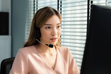 Competent female operator working on computer and while talking with clients. Concept relevant to both call centers and customer service offices.