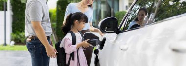 Progressive young happy family with electric vehicle and home backyard charging station. Green and clean energy from electric vehicles for healthy environment. Eco power from renewable source.