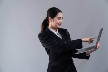 Kendine güvenen genç iş kadını izole edilmiş bir zeminde duruyor ve resmi siyah takım elbiseyle dizüstü bilgisayarda çalışıyor. Ofisteki kadın ya da yönetici, zeki ve profesyonel görünümlü. Coşkulu.