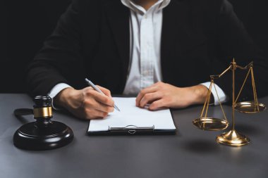 Adalet sembolleri, tokmak çekiç ve terazinin avukatın bulanık arkaplanına odaklanması ya da hukuk sisteminin dürüstlüğü ve adilliği için yasal belgeyi masasında imzalaması. denge