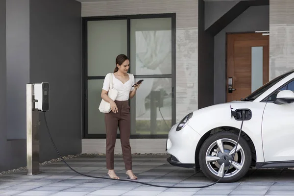 Progressive Asian Woman Holding Smartphone Electric Car Home Charging Station — Foto Stock