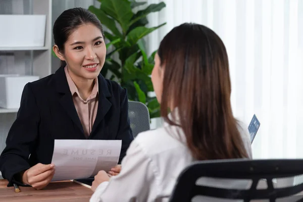 Two asian women conduct job interview in office. Applicants wear formal suit while talking about her CV and job application. Interviewer ask inquiry in positive and conversational manner. Enthusiastic