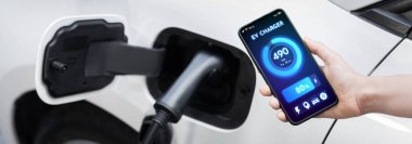 Battery status of electric vehicle displayed on smartphone application or software while vehicle is plugged into charging station for progressive future refueling. Battery status on phone screen.