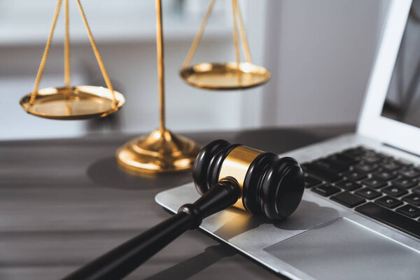 Symbolizing justice and legal authority, golden balanced scale and gavel on desk with laptop in law office background, reflecting concept of equality and fair judgment by lawyer and judge. equility