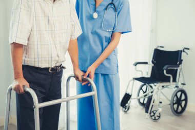 Physiotherapist assists her contented senior patient on folding walker. Recuperation for elderly, seniors care, nursing home.