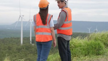 Erkek ve kadın mühendisler kırsal kesimdeki bir tepenin tepesinde ya da dağda rüzgar çiftliğinde çalışıyorlar. Yenilenebilir ve sürdürülebilir enerjinin gelecekteki üretimi için yenilikçi idealler.