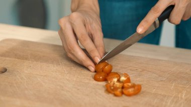 Close up hands holding a knife preparing a contented meal. Sliced tomatoes and other vegetables on the glass dish.