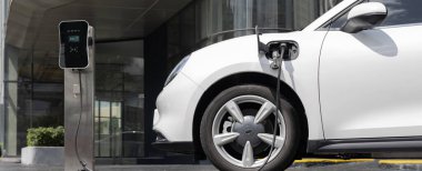 Progressive electric vehicle recharging battery at charging station powered by sustainable clean energy at city residential area. Eco-friendly vehicle concept.