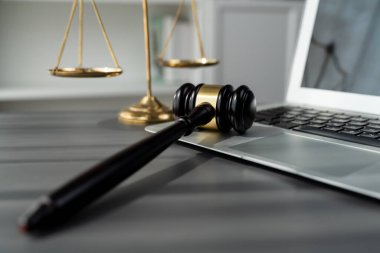 Adalet ve hukuki otoriteyi temsil eden, altın dengeli ölçek ve hukuk bürosunda dizüstü bilgisayarlı tokmak, avukat ve hakimin eşitlik ve adil yargılama kavramını yansıtıyor. denge